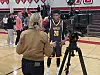 Tavid Johnson, center, a junior at San Diego's Francis Parker High School, gets interviewed by a television reporter as UNM Lobos head coach Eric Olen, second from left in red, and Lobo freshman Jake Hall, far left, talk nearby after a high school basketball game in Solana Beach, California, on Friday, Jan. 16, 2026.