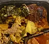 Close-up of a takeout container filled with mixed stewed greens and meats.