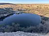Deep circular lake ringed by brush and cliffs in a dry desert landscape