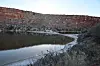 Curving shoreline of a small lake beneath red rock cliffs at dusk