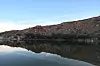 Calm desert lake reflecting rocky red cliffs under a clear sky.
