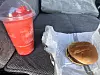 McDonald’s hamburger on wrapper beside a red frozen drink on a car seat.