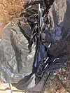 Broken tent poles leaning against a crumpled black tarp on dry ground outdoors.