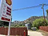 Shell gas price sign beside a rural road with hills and power lines in the background