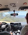 View from back seat of a car driving on a mountain road with navigation screen visible