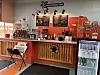Coffee shop counter with menu boards, a service area, and a refrigerator stocked with drinks.