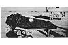 Black-and-white image of a tarp-covered object strapped to a flatbed outdoors.