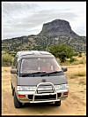 Modified Toyota van parked on a dirt road with a desert mesa in the background.