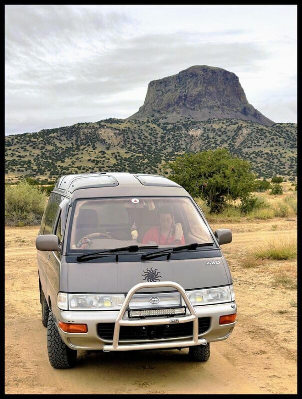 Modified Toyota van parked on a dirt road with a desert mesa in the background.