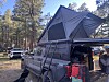 A pickup truck fitted with a rooftop tent and camping gear parked among pine trees.