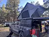 A pickup truck fitted with a rooftop tent and camping gear parked among pine trees.