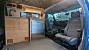 Inside a camper van with wood cabinets, a small fridge, and two front seats.
