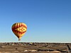 A red and yellow hot air balloon floating over a barren desert landscape.