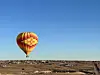 A red and yellow hot air balloon floating over a barren desert landscape.