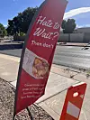 Red Blake's roadside banner advertising grab-and-go breakfast burritos stands beside a street and sidewalk.