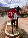 Red stop sign reading 'Pay here' beside a paved road with red rock cliffs and blue sky.