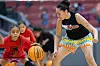 A coach crouches in a defensive stance as a young girl dribbles a basketball during an indoor camp.