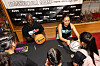 Two basketball players sign balls for children at a camp table with a branded backdrop behind them.