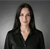 Portrait of a woman with long dark hair wearing a black blouse against a gray backdrop.