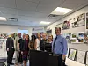 A group of adults poses around a podium in a Saranam office with photos and posters on the walls.