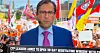ESPN's Pete Thamel reporting during the Sept. 5 broadcast of ESPN College Game Day on Saturday, Sept. 12, 2026, in Austin Texas while in the background are dozens of signs and flags, including New Mexico's state flag and a red UNM Lobos flag being waved by Valerie Flores.