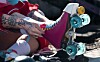 Close-up of a skater tying bright pink roller skates with turquoise wheels at a boot camp.